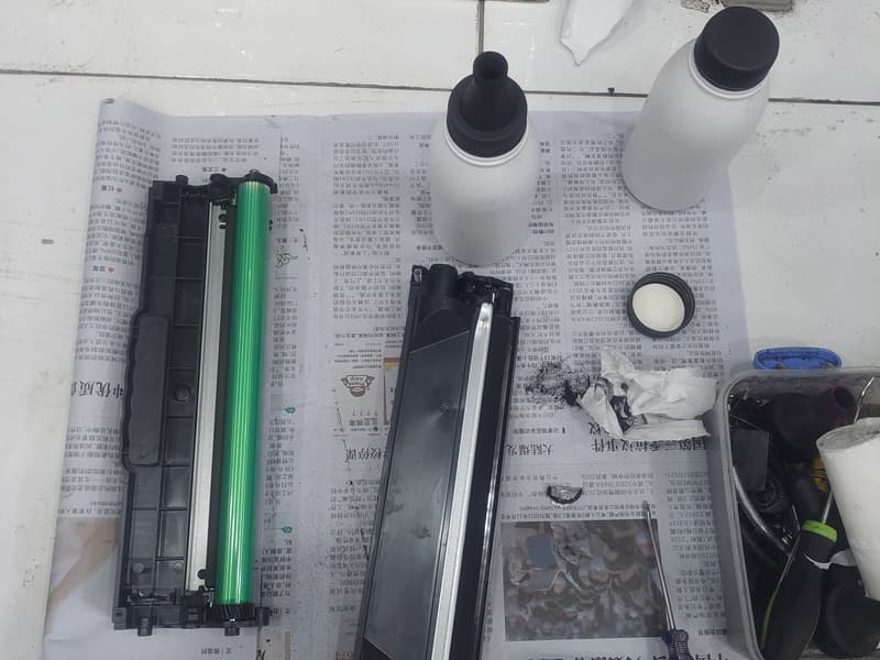 Hộp mực tháo rời thành hai khoang cùng chai mực mới, đặt trên giấy lót